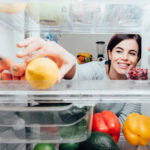 smiling woman reaching into a refrigerator for a lemon