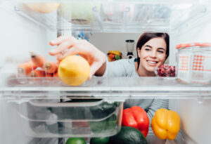 smiling woman reaching into a refrigerator for a lemon
